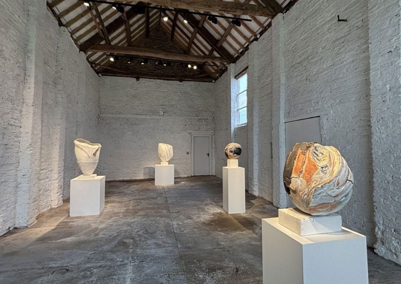 A whitewashed barn gallery with sculptures on white plinths under old timber beams
