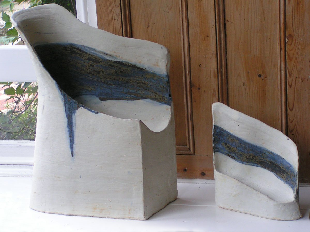 Two white forms with a band of blue glaze, on a windowsill