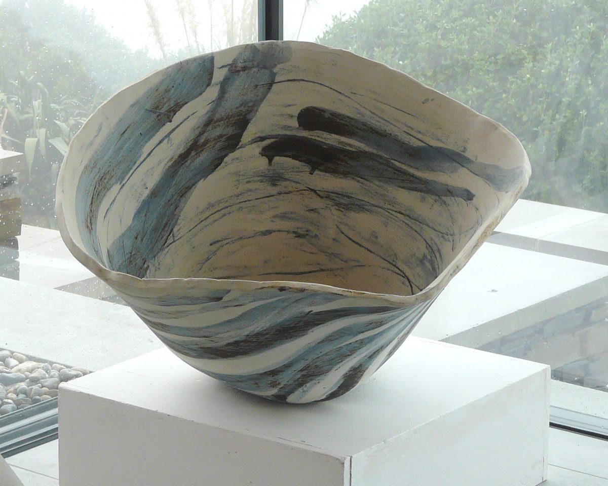 A wide bowl with blue and black brushwork inside and out, on a white plinth by a window