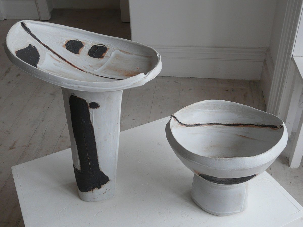 A tall dish and a footed bowl, painted white with black marks, on a white plinth