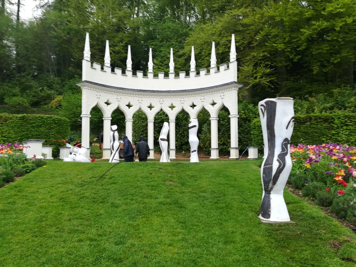 Black and white vessels placed among the arches of a white garden pavilion, with tulips in the foreground