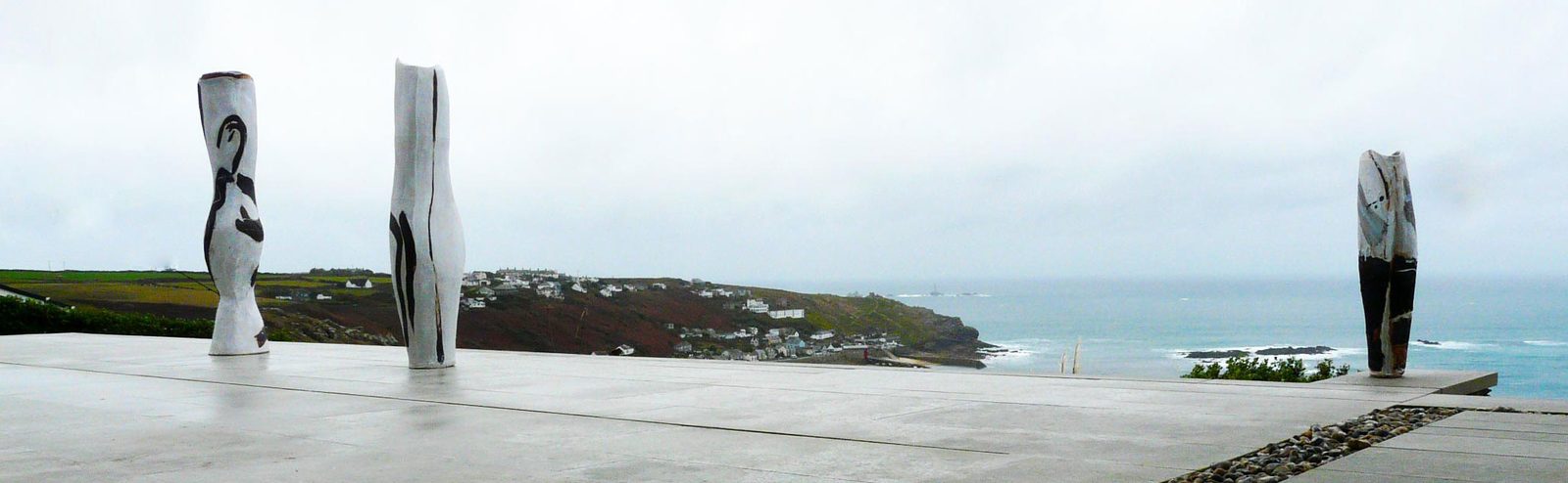 Three tall vessels with black brushwork on a stone terrace above the sea and a coastal village